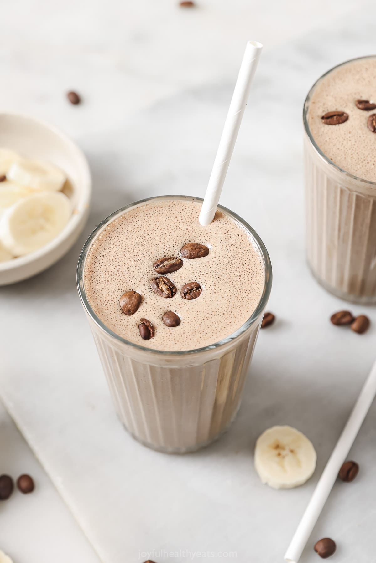 Creamy coffee smoothie in a tall glass with coffee beans on top. 