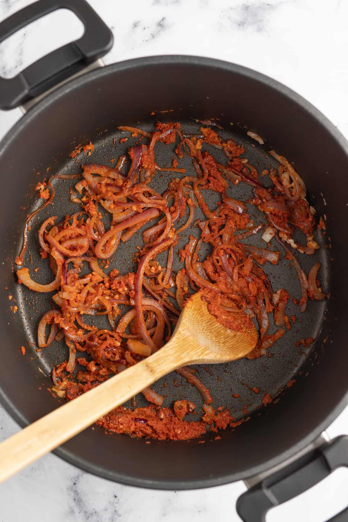 stirring curry into a pot with sliced onions