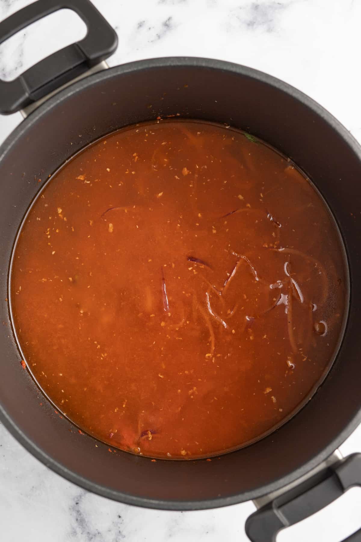 This easy Thai Chicken Noodle Soup is an epic homemade soup recipe that only takes 30 minutes to make. It's a simple and authentic recipe! a red brothy sauce in a large pot