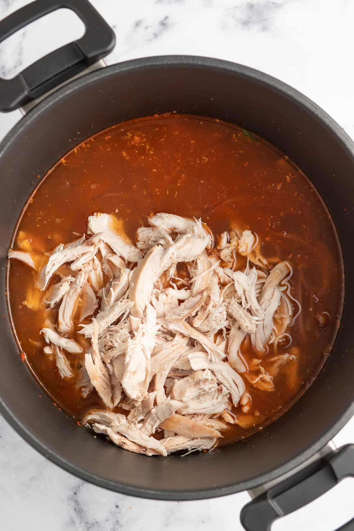 putting shredded chicken into a large pot with a light red broth sauce