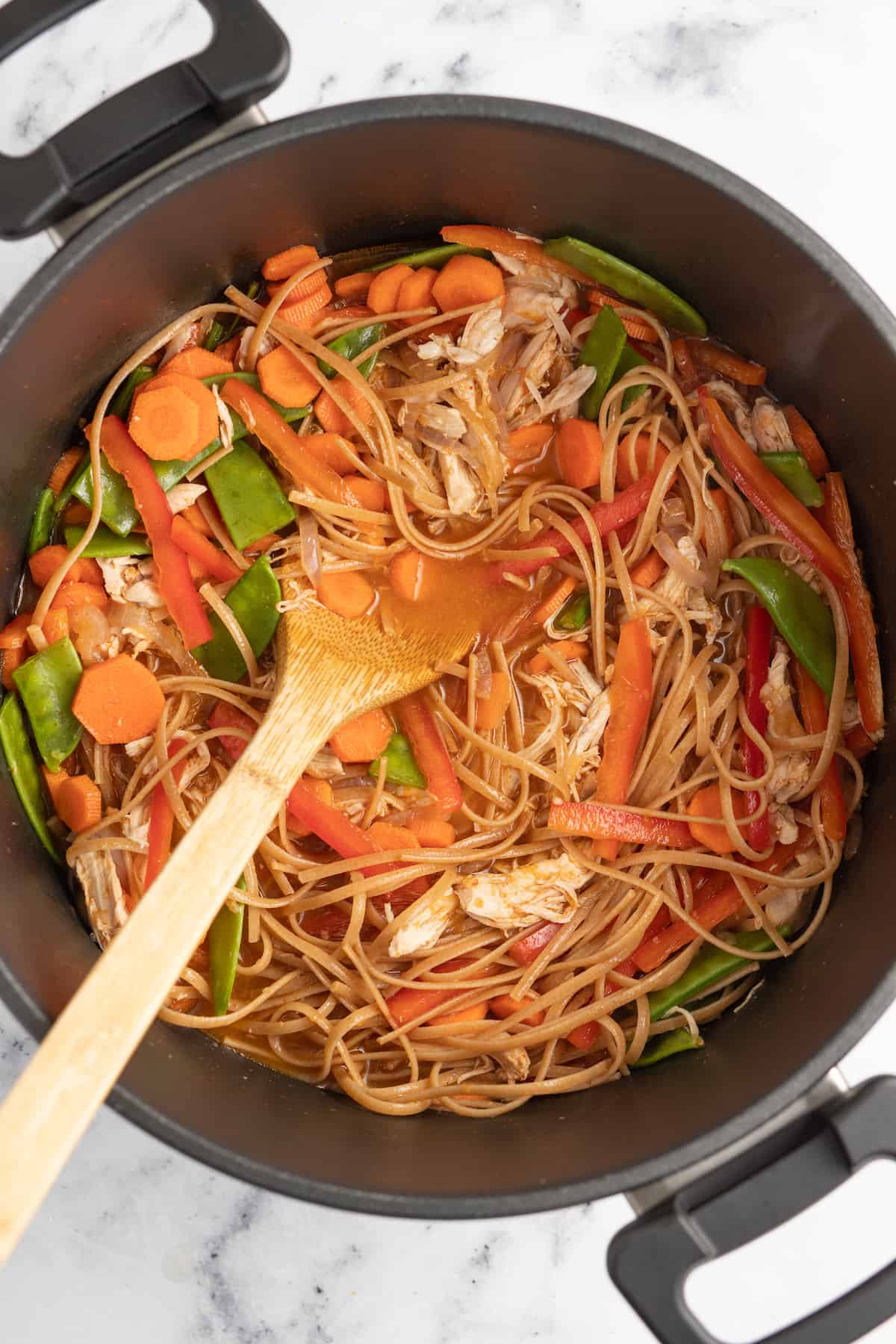 stirring vegetables into rice noodles in a large pot