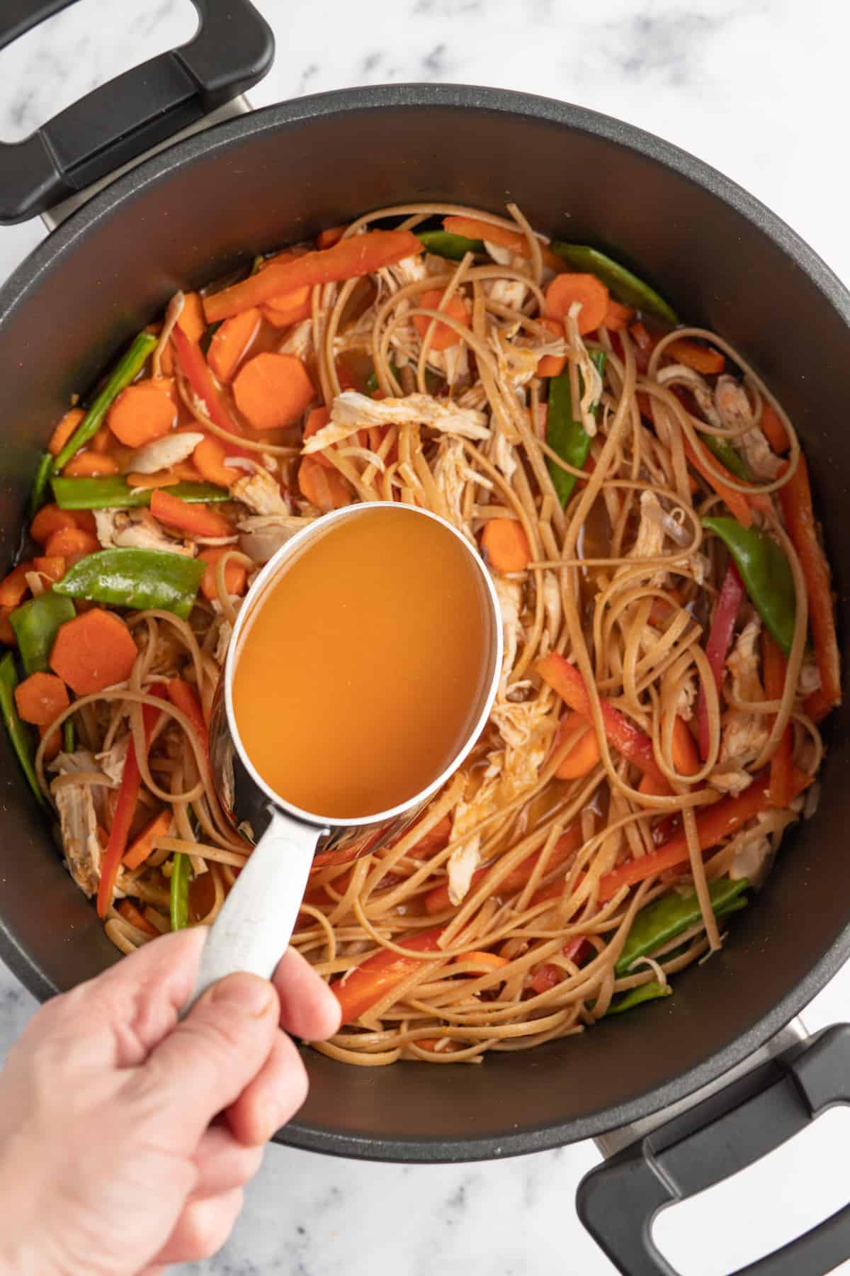 a measuring cup with broth over a pot of noodles and vegetables