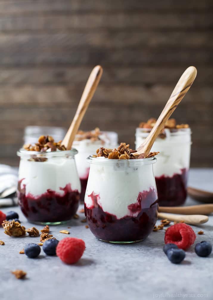 Jars of Fresh Yogurt Parfait with a Mixed Berry Compote and crunchy vanilla almond granola with a wooden spoon in each