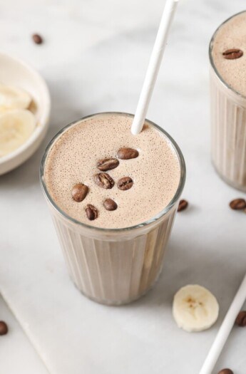 Creamy coffee smoothie in a tall glass with coffee beans on top.