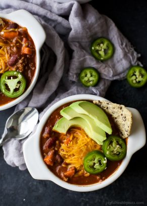 Beef Chili topped with cheese, avocado and jalapenos in a white bowl