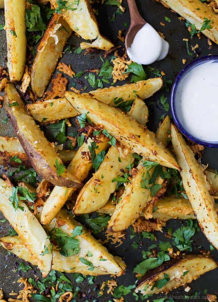 Garlic Parmesan seasoned Potato Wedges on a baking sheet with a cup of creamy sauce