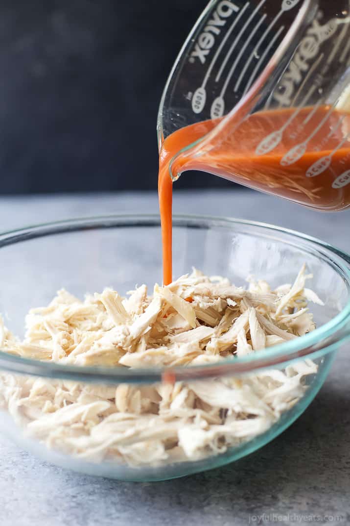 Buffalo sauce being poured over a bowl of shredded chicken