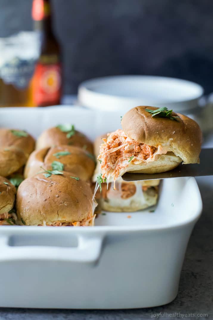 A spatula removing a buffalo chicken slider from a baking dish