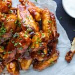 Sweet and spicy chicken wings piled onto a piece of parchment paper with an empty bone beside them