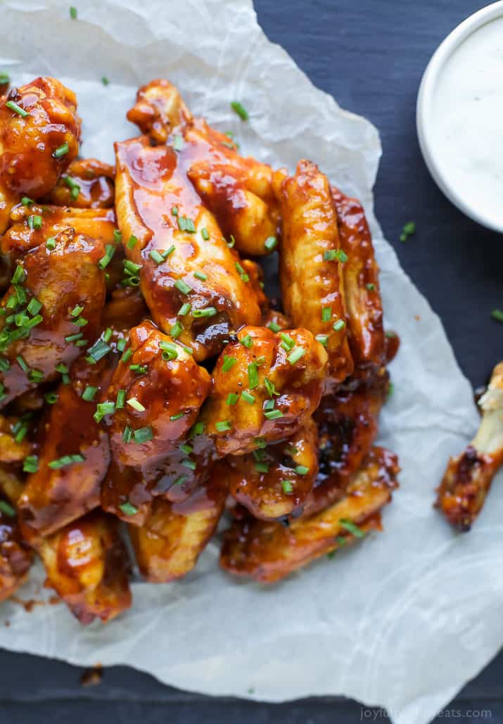 Sweet and spicy chicken wings piled onto a piece of parchment paper with an empty bone beside them