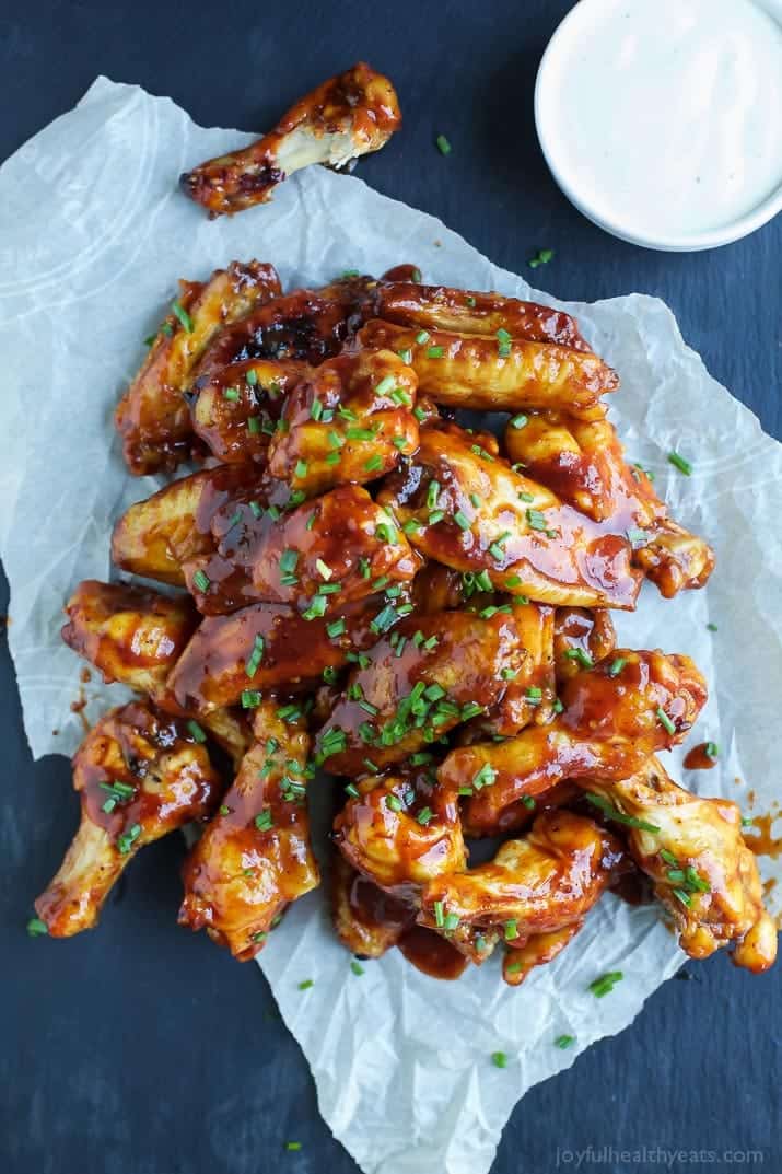 Baked chicken wings piled onto a piece of parchment paper with a small bowl of ranch beside them