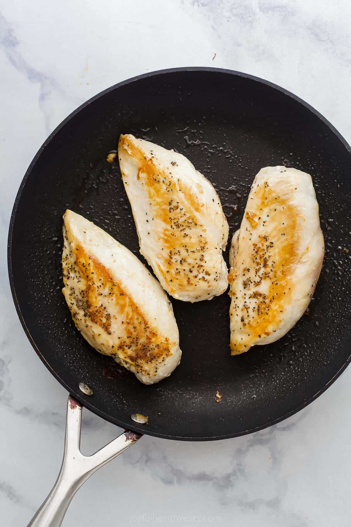three chicken breasts being seared in a cast ion skillet