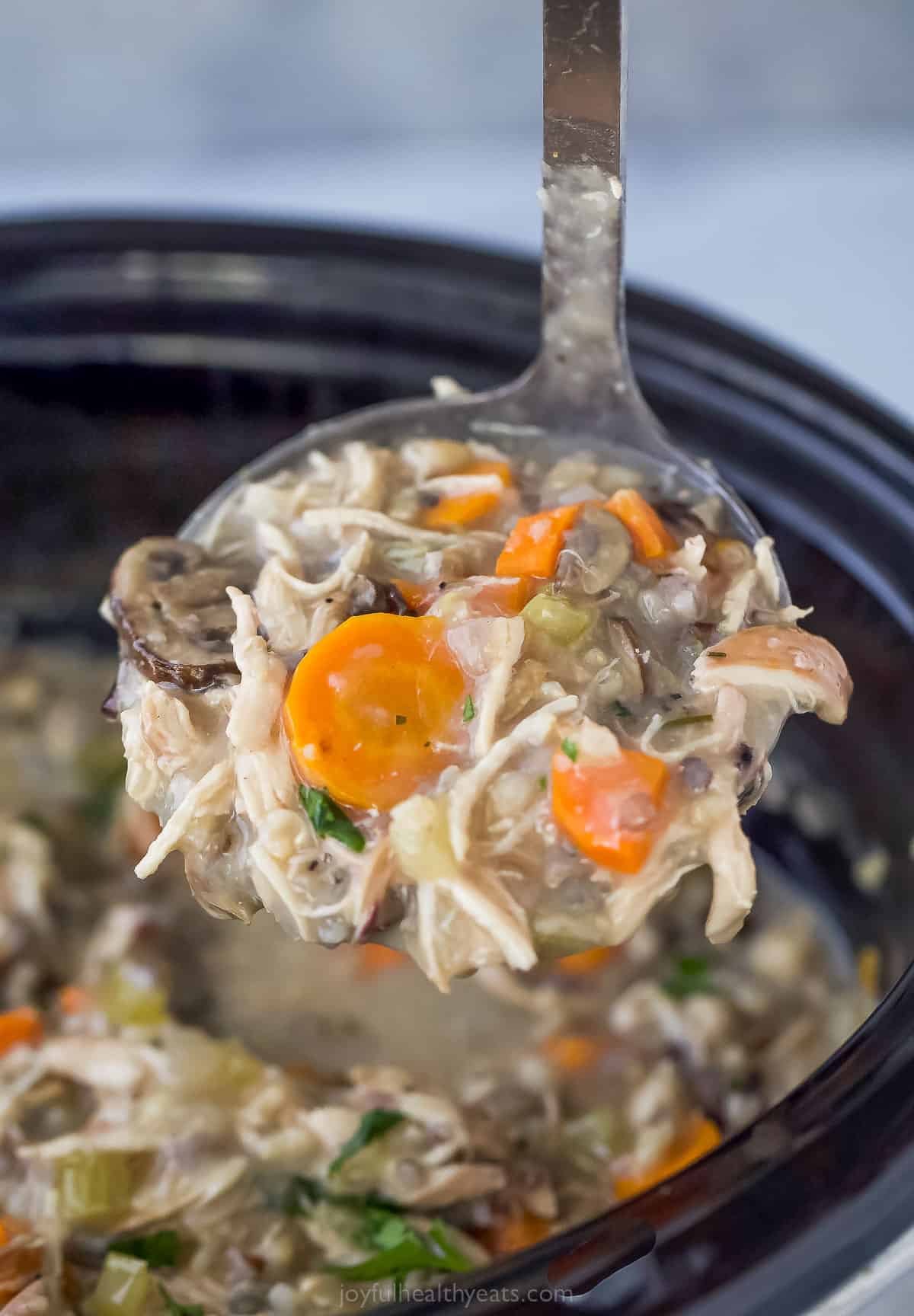 This creamy Crockpot Chicken and Wild Rice Soup is filled with wild rice, tender chicken, and veggies. Only 5 minutes of prep time! a ladle of chicken and wild rice soup in a crock pot