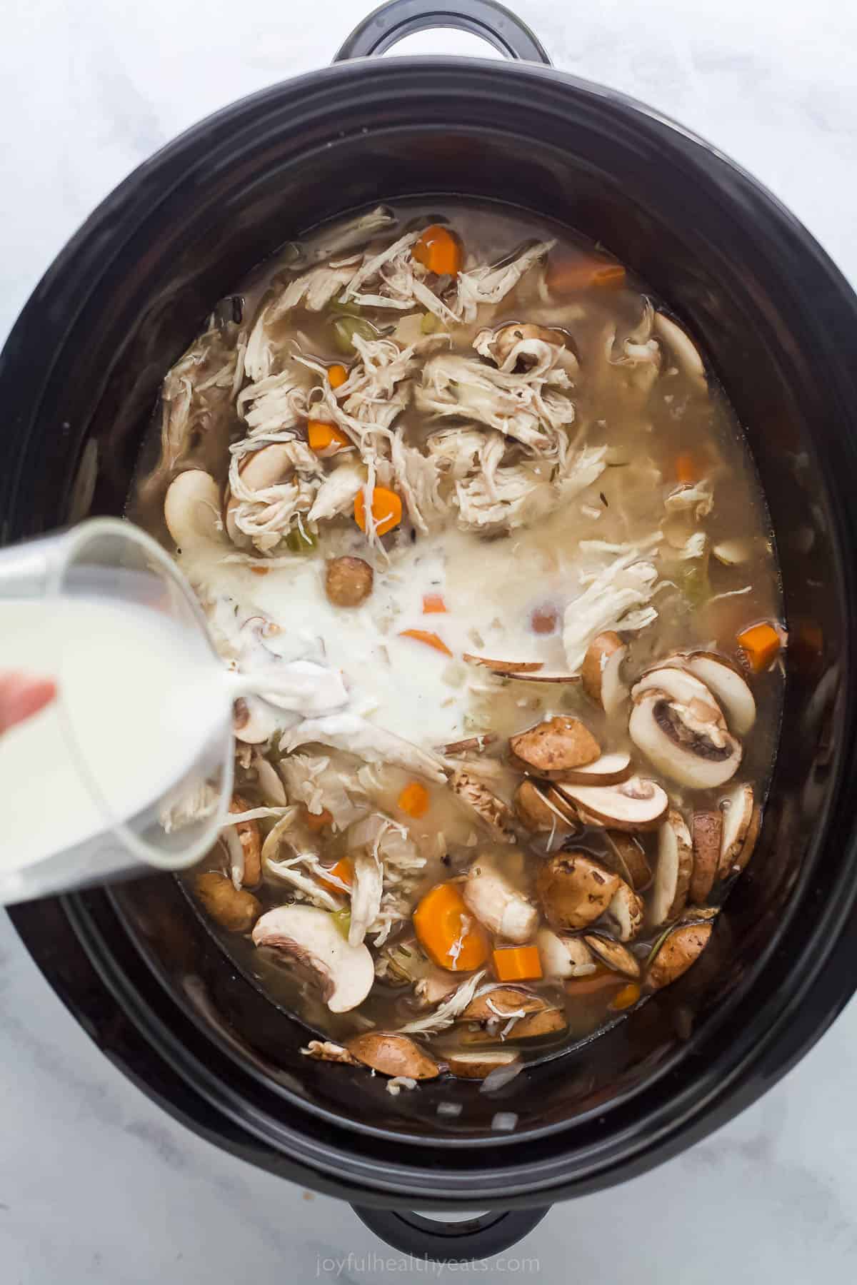 pouring cream into a chicken vegetable soup in a crock pot