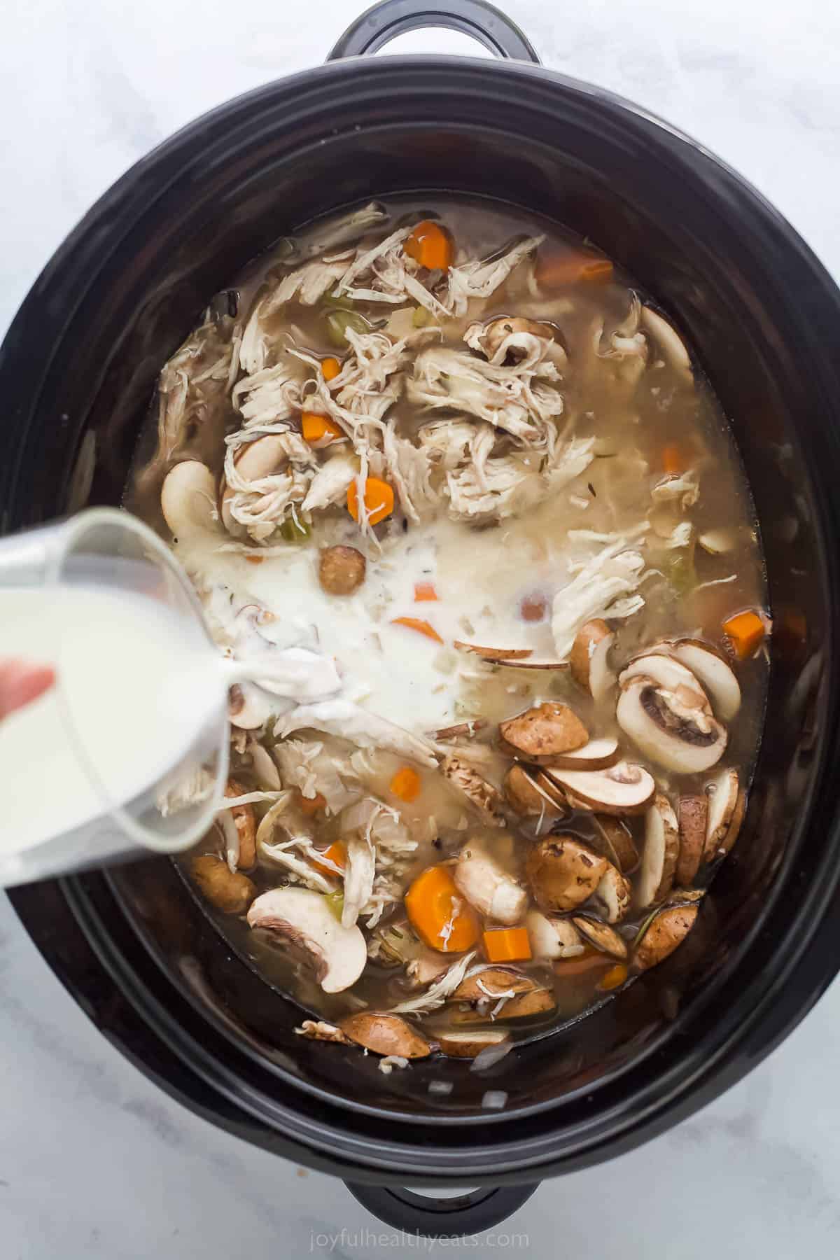 This creamy Crockpot Chicken and Wild Rice Soup is filled with wild rice, tender chicken, and veggies. Only 5 minutes of prep time! pouring cream into a chicken vegetable soup in a crock pot