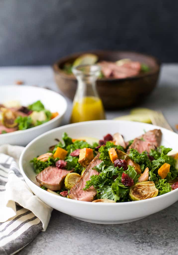 Two bowls of Harvest Steak Salad with autumn vegetables next to a carafe of homemade vinaigrette dresing 