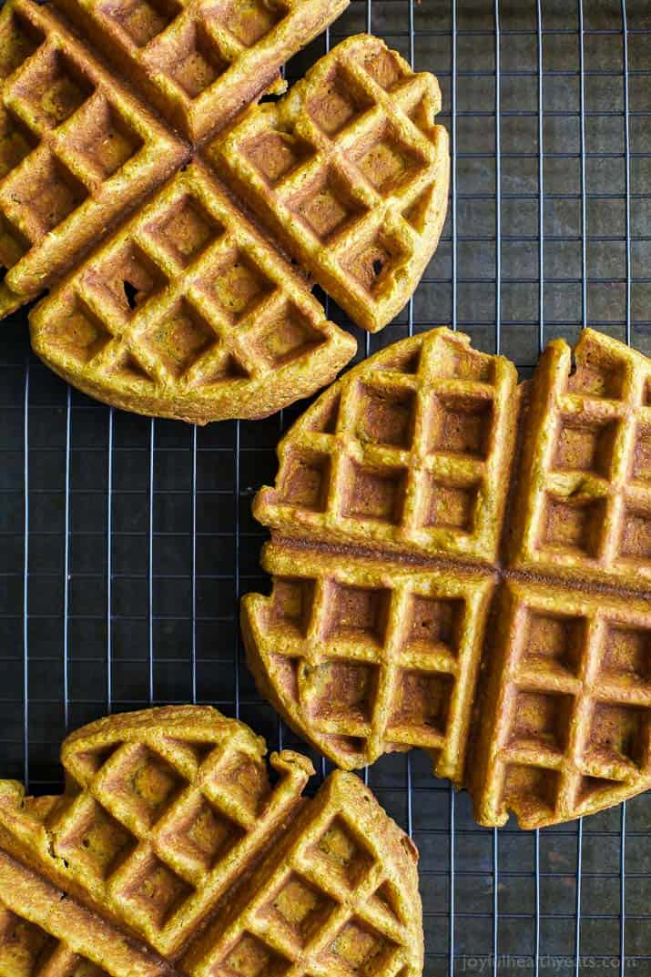 Three pumpkin waffles sitting on top of a wire cooling rack with a grid pattern
