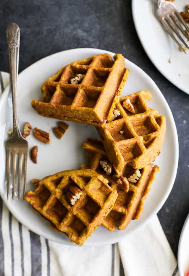 A waffle broken into four sections on a plate with a few chopped pecans and a fork