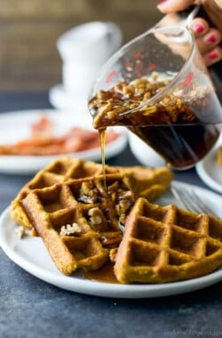 Vanilla pecan maple syrup being poured onto three quarters of a waffle