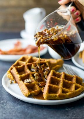 Vanilla pecan maple syrup being poured onto three quarters of a waffle