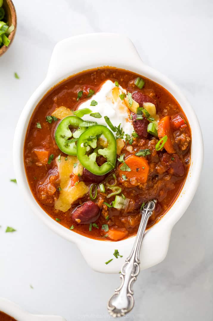 A crock bowl filled with beef chili and toppings.