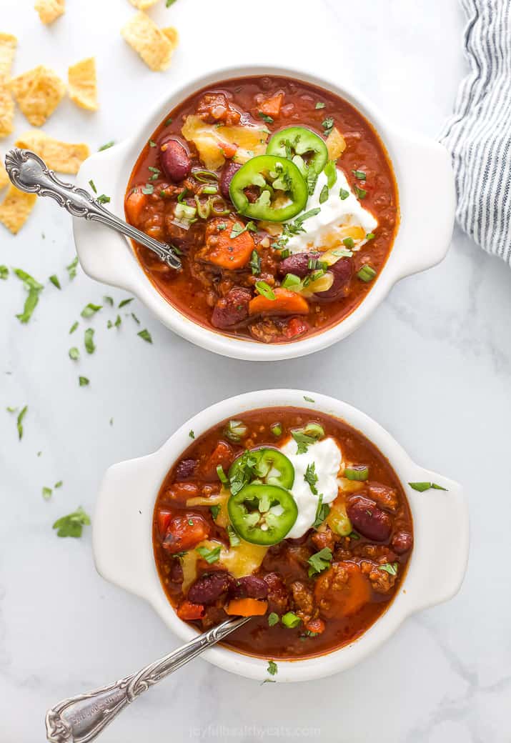 two bowls filled with beef chili and loaded with chili toppings