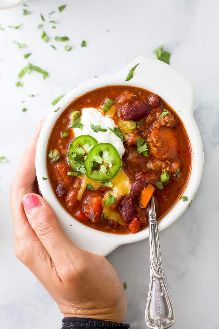 A hand holding a bowl filled with beef chili.