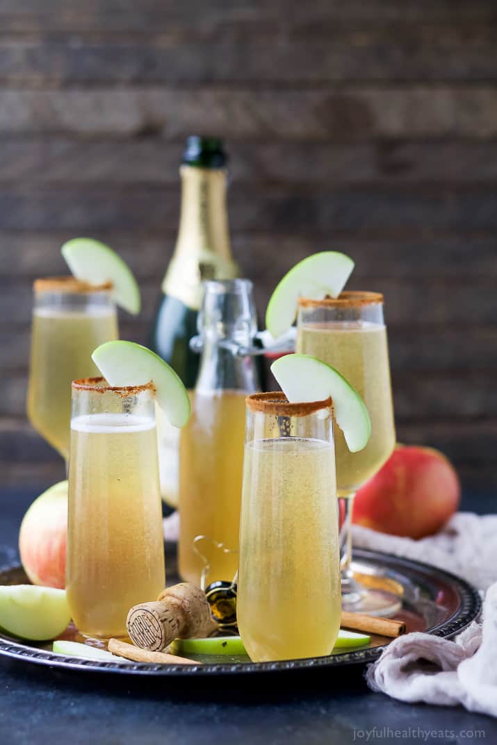 Apple cider mimosas on a serving tray garnished with apple slices.