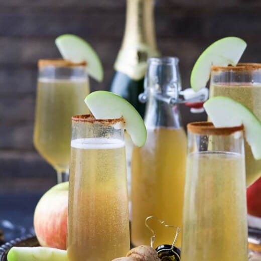 Apple cider mimosas on a serving tray garnished with apple slices.