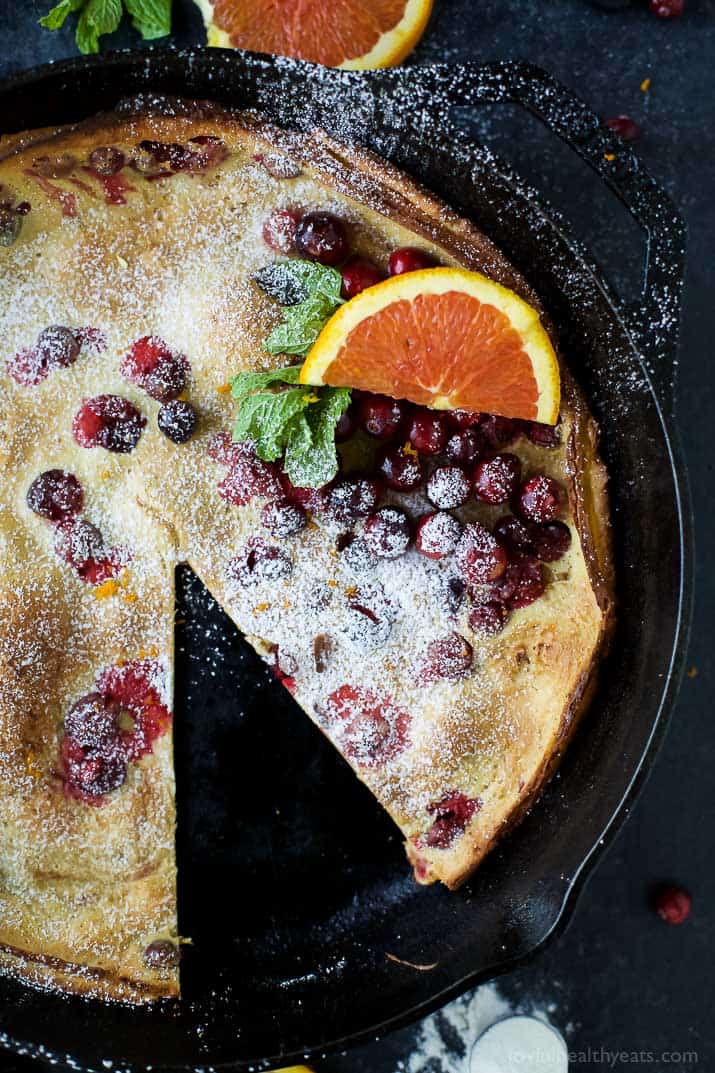 Cranberry Orange Dutch Baby in a cast-iron skillet with one slice removed