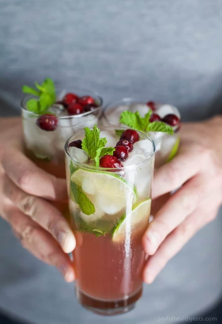 A person holding three glasses of Holiday Cranberry Mojito