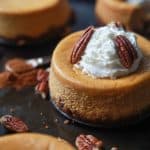 A close-up shot of a mini pumpkin cheesecake topped with whole pecans and whipped cream