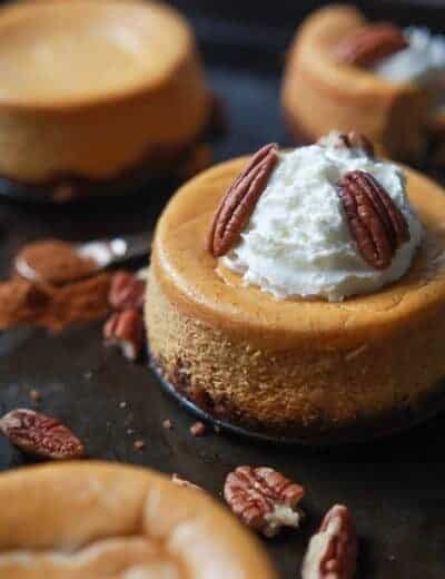 A close-up shot of a mini pumpkin cheesecake topped with whole pecans and whipped cream