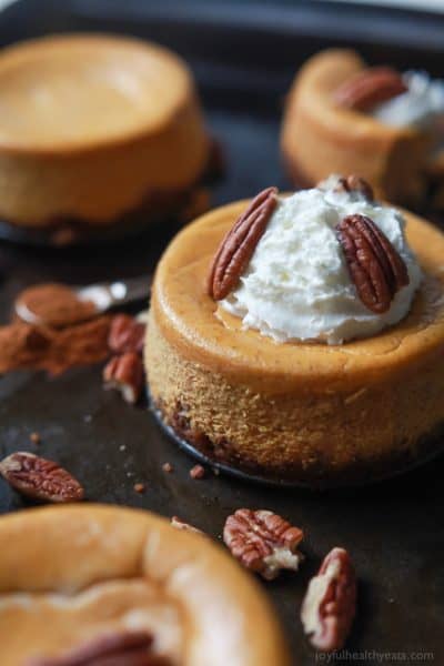 A close-up shot of a mini pumpkin cheesecake topped with whole pecans and whipped cream