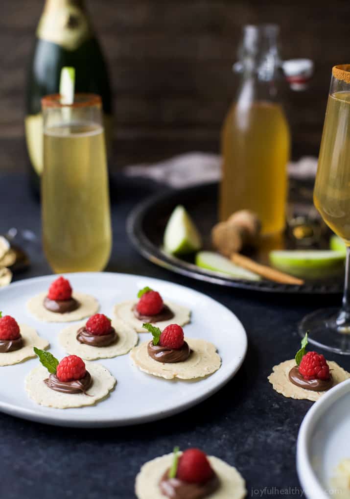 A Plate Holding Six Sweet Appetizer Bites Next to Twp Loose Bites and a Few Glasses of Champagne