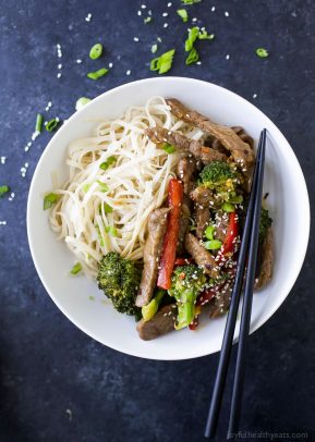 An overhead shot of a stir fry in a shallow bowl with rice noodles and a pair of chopsticks
