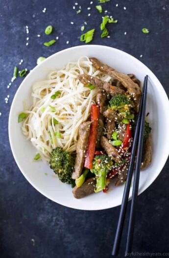 An overhead shot of a stir fry in a shallow bowl with rice noodles and a pair of chopsticks