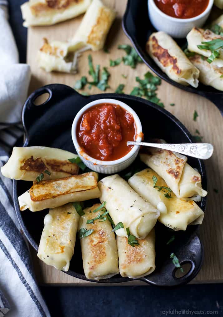 Skinny Baked Mozzarella Sticks wrapped in wonton wrappers in a cast-iron pan with a cup of marinara sauce