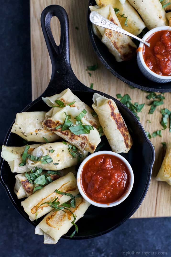 Skinny Baked Mozzarella Sticks wrapped in wonton wrappers in a cast-iron skillet with a cup of marinara sauce