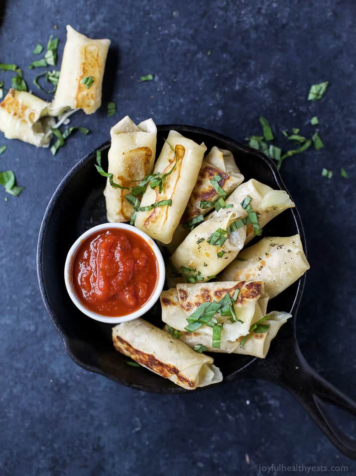 Top view of Skinny Baked Mozzarella Sticks wrapped in wonton wrappers with a cup of marinara sauce