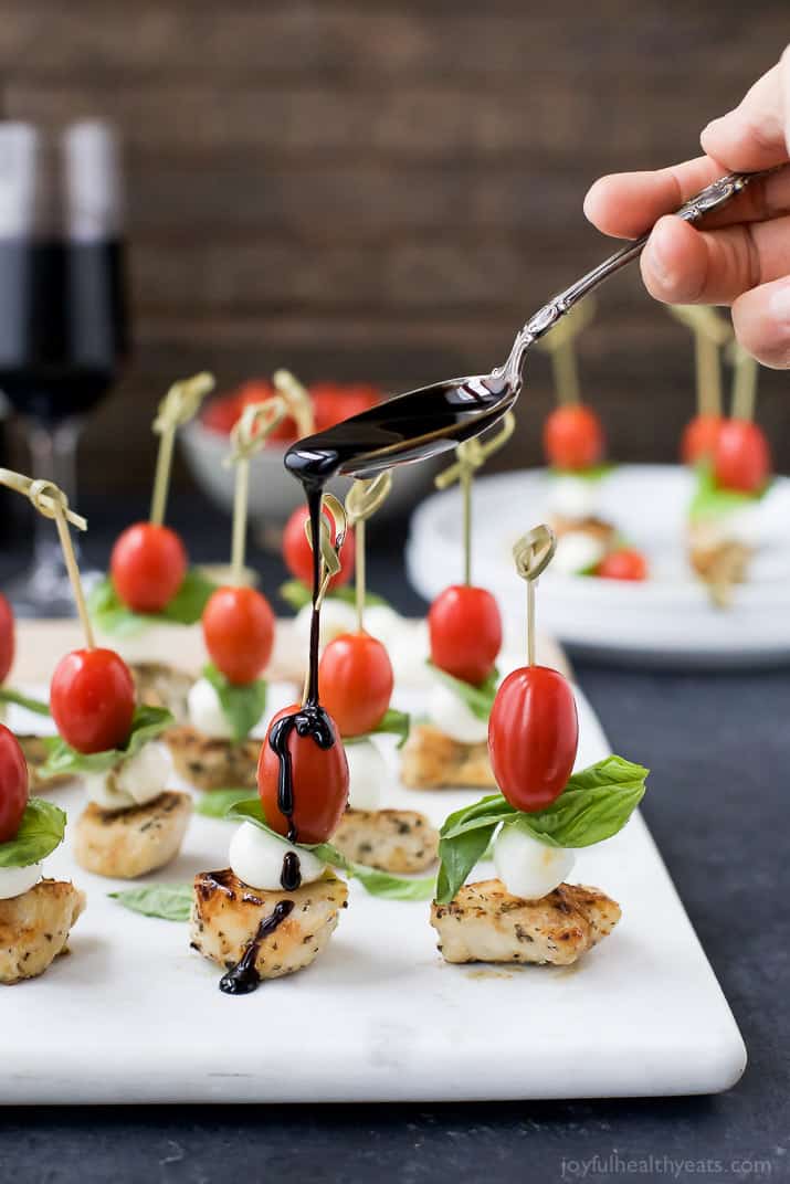 Caprese Chicken Skewers on a cutting board being drizzled with a homemade Balsamic Glaze