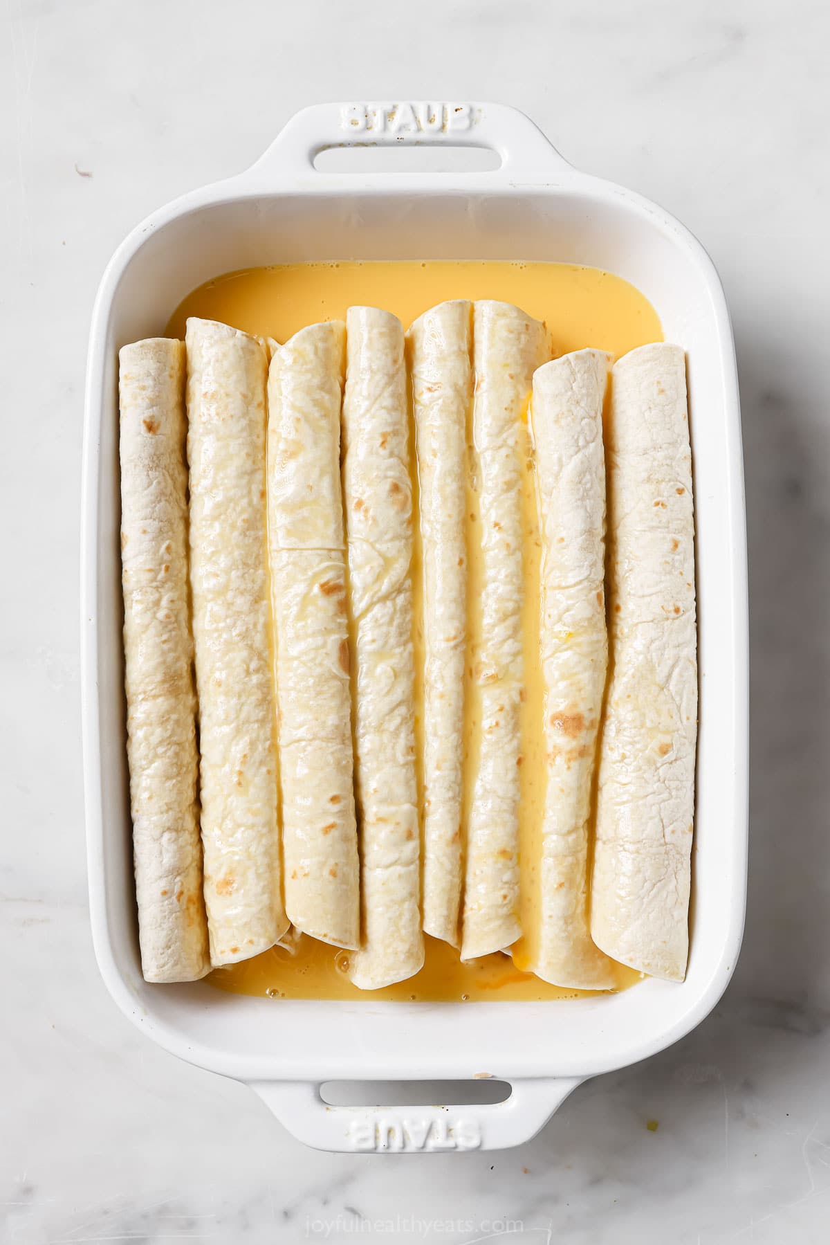 Pouring the egg mixture over the enchiladas. 