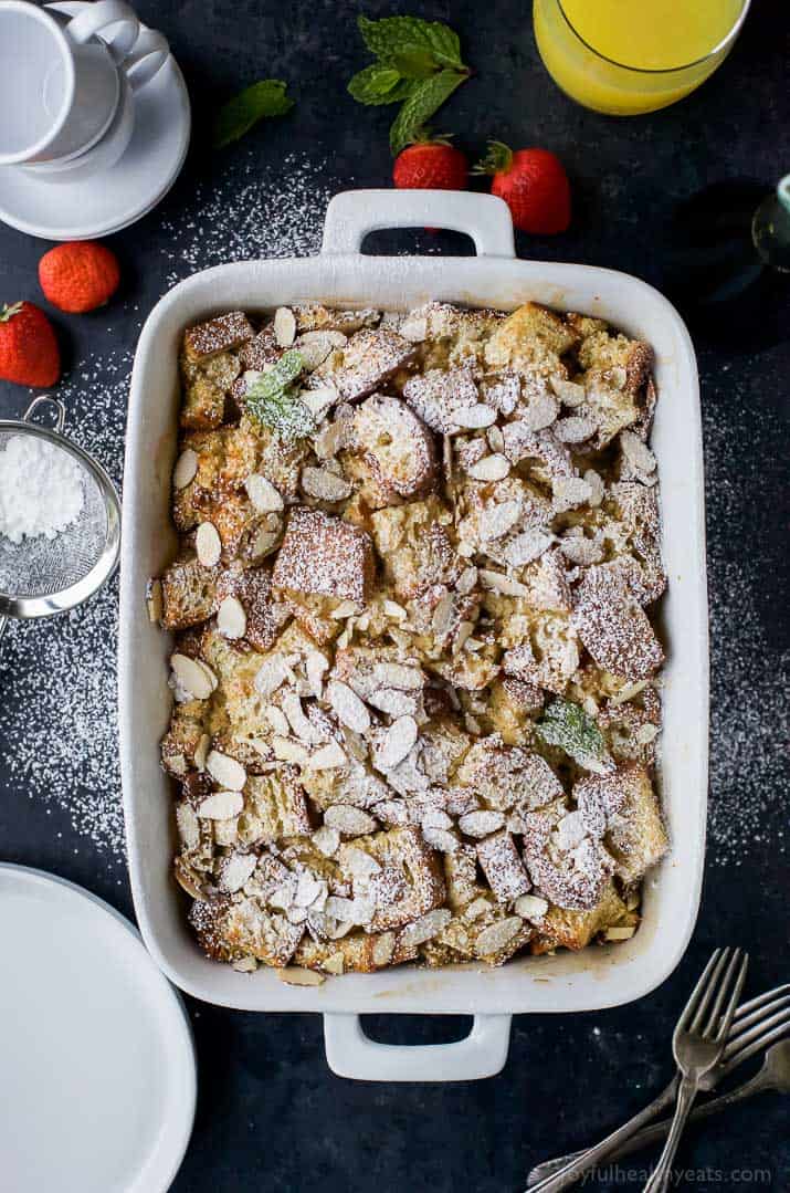 A French toast casserole topped with a dusting of powdered sugar in a large baking dish with handles