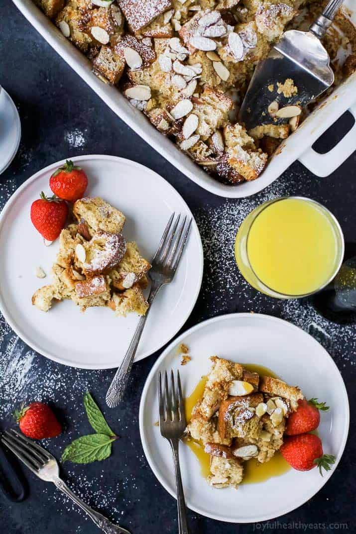 A freshly-baked French toast casserole in a pan with two individual servings on small plates beside it