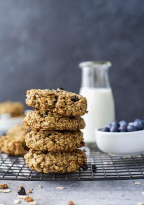 Four blueberry oatmeal cookies stacked on top of each other with a bowl of fresh berries in the background