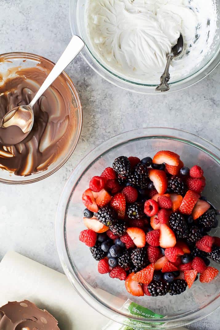 Top view of bowls of melted chocolate, coconut whipped cream, and fresh berries