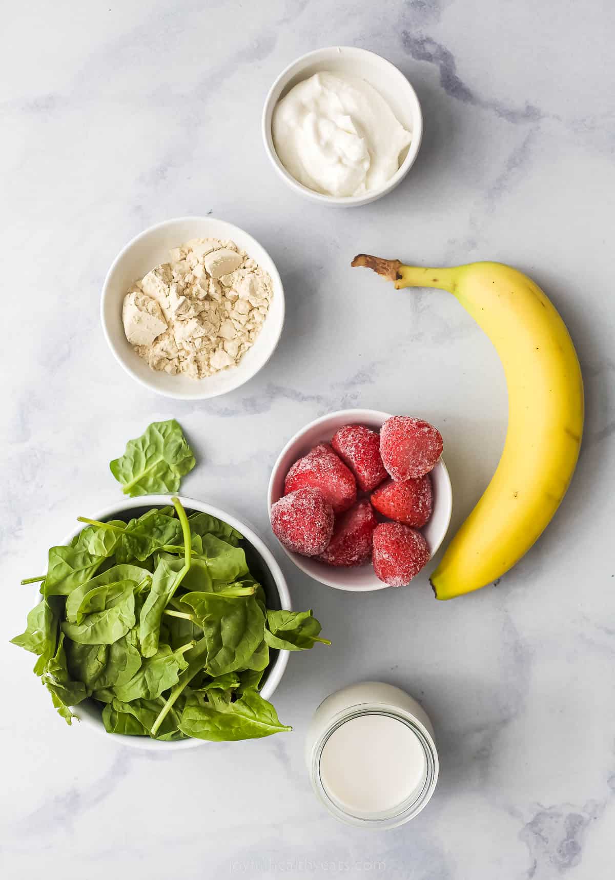 a bowl of spinach, banana, protein powder, frozen starwberries, and yogurt on a counter