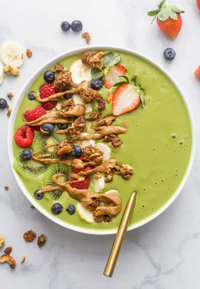 green smoothie bowl with banana slices, strawberries, granola, and peanut butter drizzle