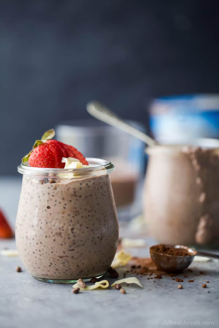 A glass of Coconut Dark Chocolate Chia Pudding topped with fresh strawberries and coconut