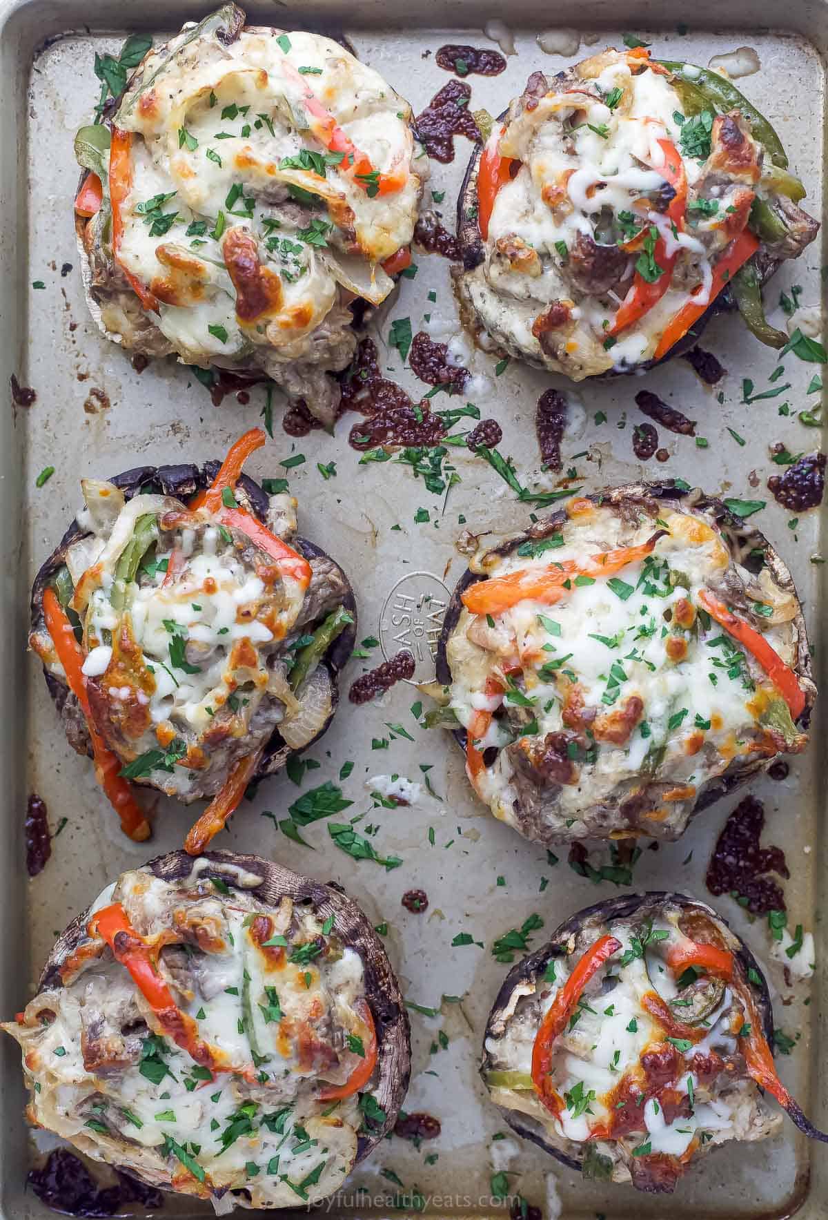 These Easy 30-Minute Philly Cheese Steak Stuffed Mushrooms are packed with tender steak, sautéed vegetables, and gooey cheese. philly cheesesteak stuffed mushrooms on a sheet tray garnished with fresh herbs
